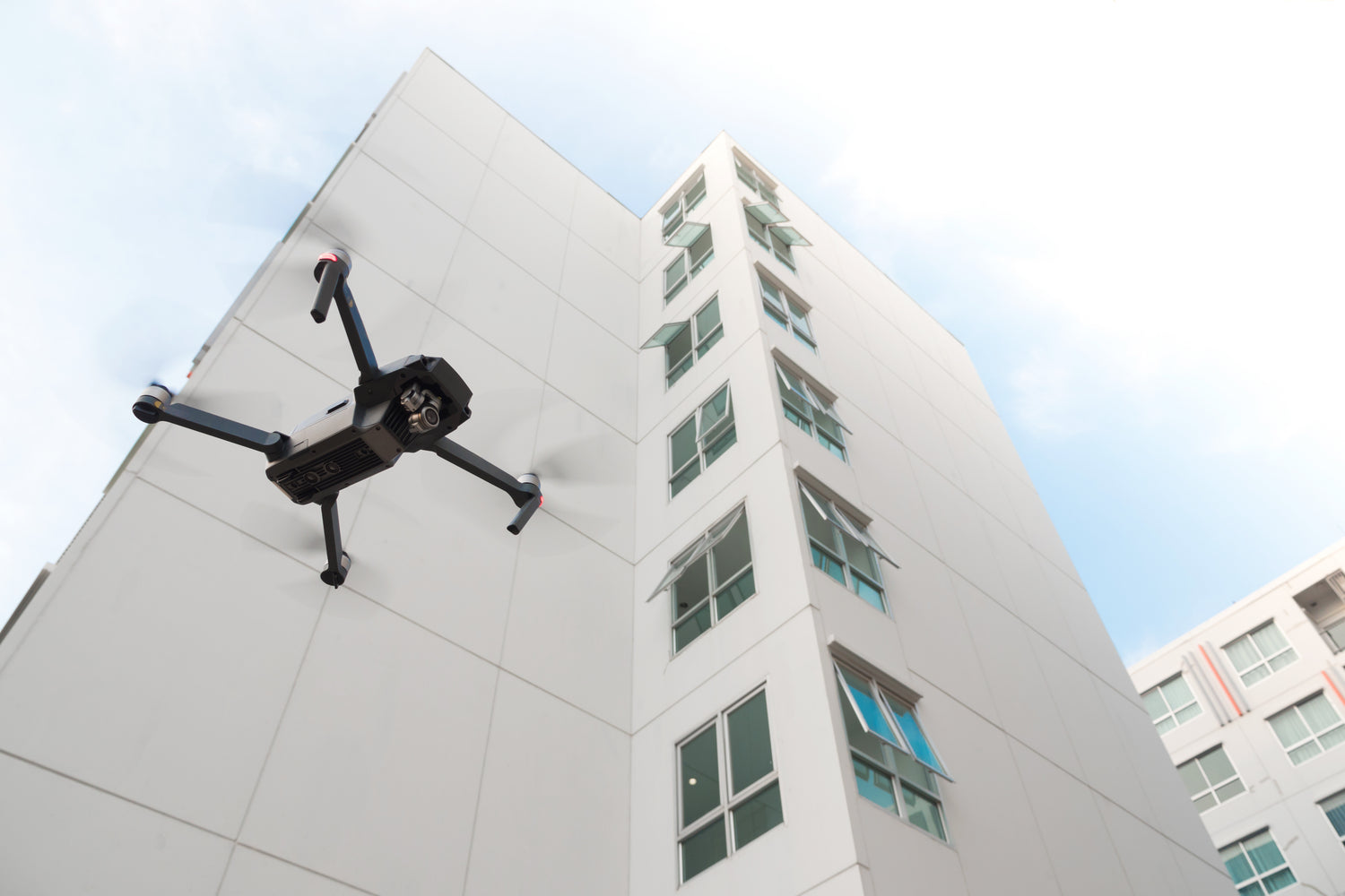 Drone passing high above next to building.